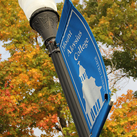 Mount Aloysius sign on lamp post in front of fall foliage Residence Halls at Mount Aloysius