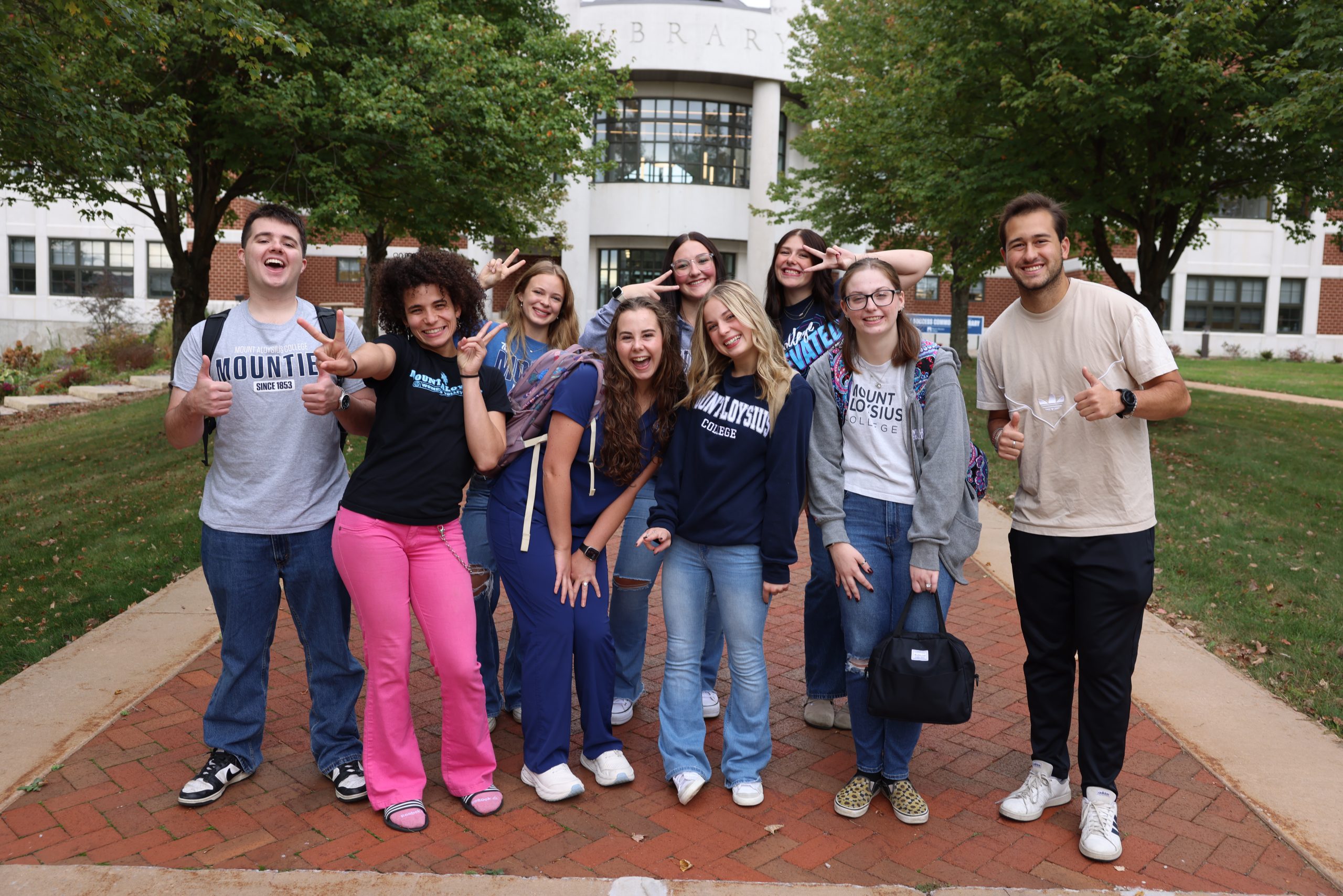 Group of Mountie students smile to the camera in front of the library